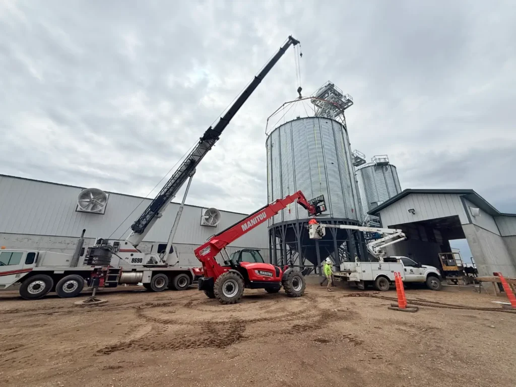 Mobile crane and telehandler forklift performing heavy lifting at an industrial grain silo site